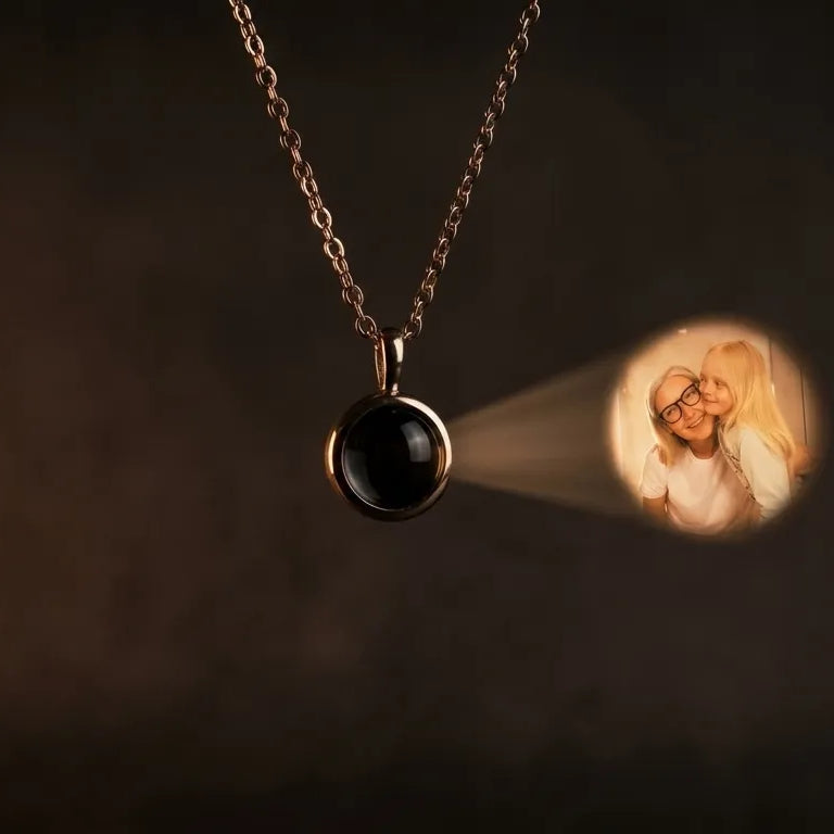 A photo projection pendant on a fine chain glowing in warm light on a dark background, showing how the hidden photo appears