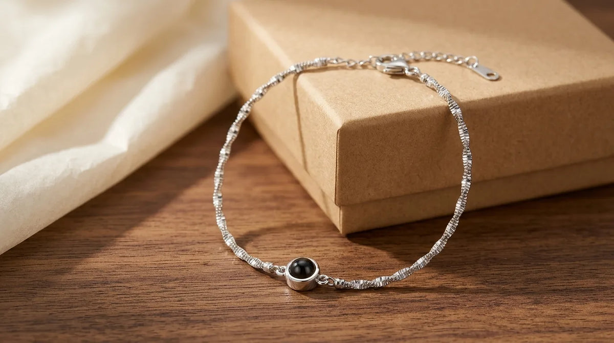 A photo projection bracelet with a deep black round lens resting on walnut beside a small kraft box